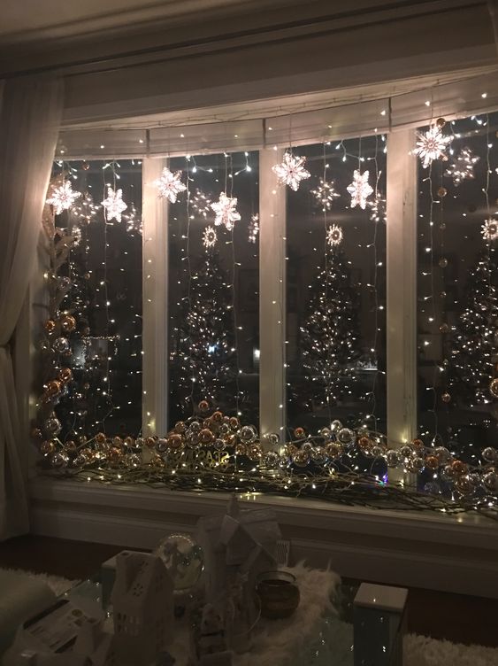 shiny Christmas window decor with lights, light stars and some silver ornaments on the windowsill