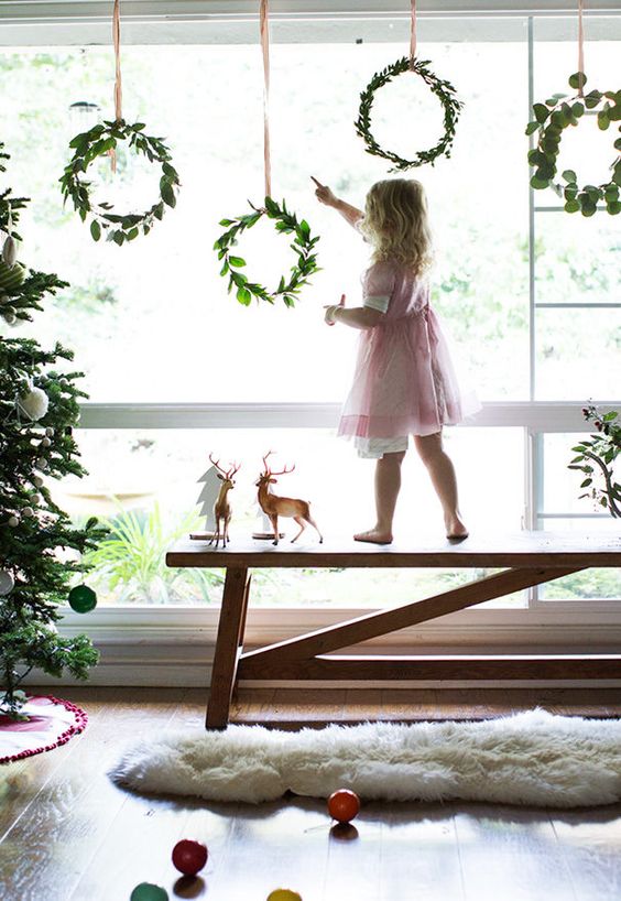 small greenery wreaths hanging on the window will make your space feel more holiday-like