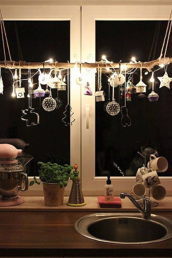 window Christmas decor of a branch with clay ornaments, cookie cutters, lights and mini houses and acupcakes is chic