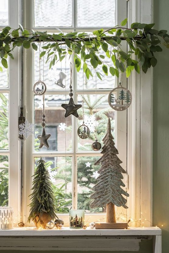 window Christmas decor with fresh greenery, silver and white ornaments, pretty wooden ornaments and mini trees