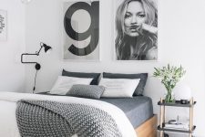 a Nordic bedroom with a bed and grey bedding, a gallery wall, a chandelier, a cart nightstand and a black sconce