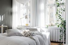 a Nordic bedroom with a soot accent wall, a bed with neutral bedding, a pendant lamp and greenery