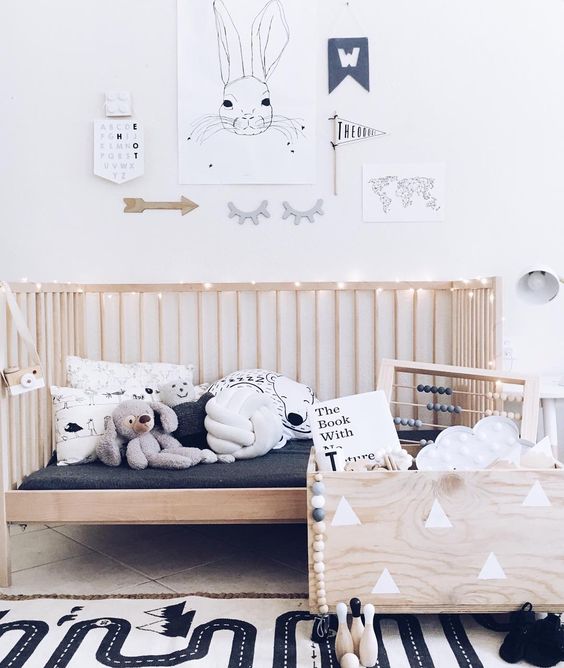 a Nordic kid’s room with a wooden bed and a wooden box for toys, a printed rug, a gallery wall with artworks and not only