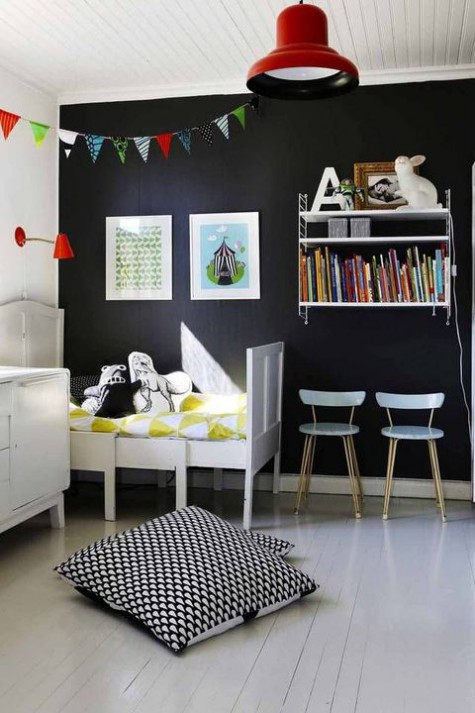 a Nordic kid’s room with vintage white furniture, a wall shelf, a black statement wall, colorful books and buntings