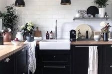 a Nordic kitchen with black cabinetry, butcherblock countertops, black pendant lamps and potted plants to refresh it