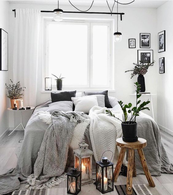 a Scandi bedroom with a bed and monochromatic bedding, a stool, mismatching nightstands, a gallery wall and candle lanterns