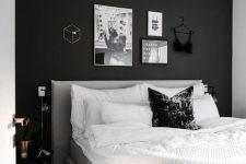a Scandi bedroom with a black accent wall, a neutral bed with neutral bedding, a gallery wall over the bed