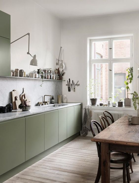 a Scandi kitchen with olive green cabinets, a grey stone backsplash and countertops, a vintage table and stained chairs