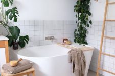 a Scandinavian bathroom clad with square tiles, an oval tub, a ladder, a rug, potted greenery is very welcoming