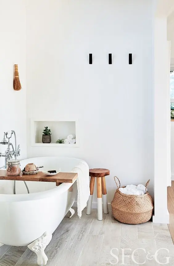 a Scandinavian bathroom with a free-standing bathtub, a niche, a stool, a basket, a shelf and some wall lamps