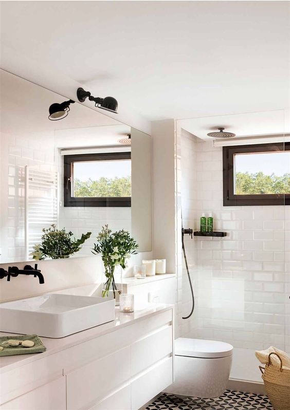 a Scandinavian bathroom with black and white tiles, a white vanity, a sink, a shower space, a black lamp and a window