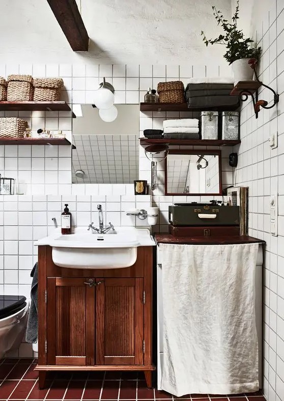 A Scandinavian bathroom with white square tiles, brown ones on the floor, a dark stained vanity and matching shelves