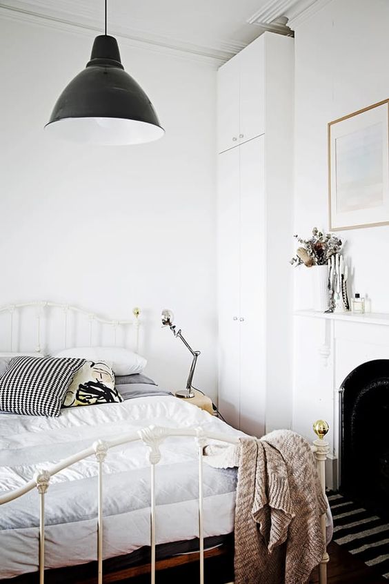 a Scandinavian bedroom with a French fireplace, a forged bed with neutral bedding, a black pendant lamp and a wardrobe