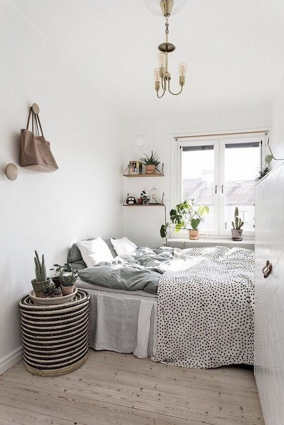 a Scandinavian bedroom with a bed and printed bedding, a woven bedside table, some shelves, a chandelier and some plants