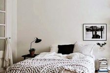 a Scandinavian bedroom with a bed, neutral bedding, an artwork, a book stack, a nightstand and some lamps