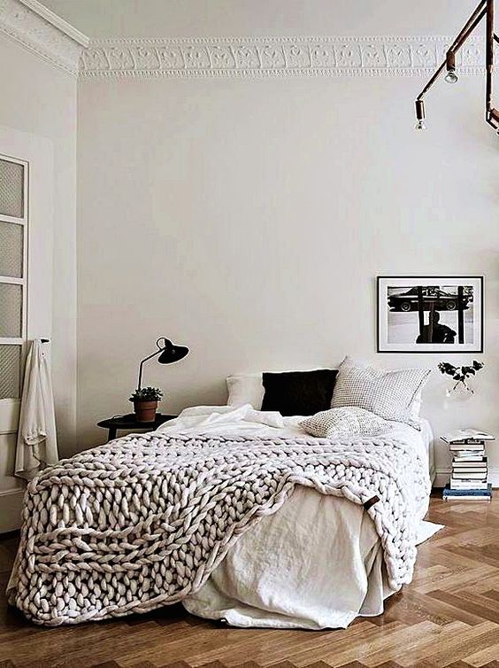 a Scandinavian bedroom with a bed, neutral bedding, an artwork, a book stack, a nightstand and some lamps