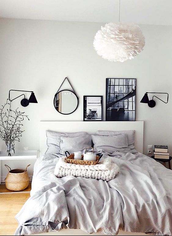 a Scandinavian bedroom with a bed styled with grey bedding, mismatching nightstands, a basket and a gallery wall on the mantel