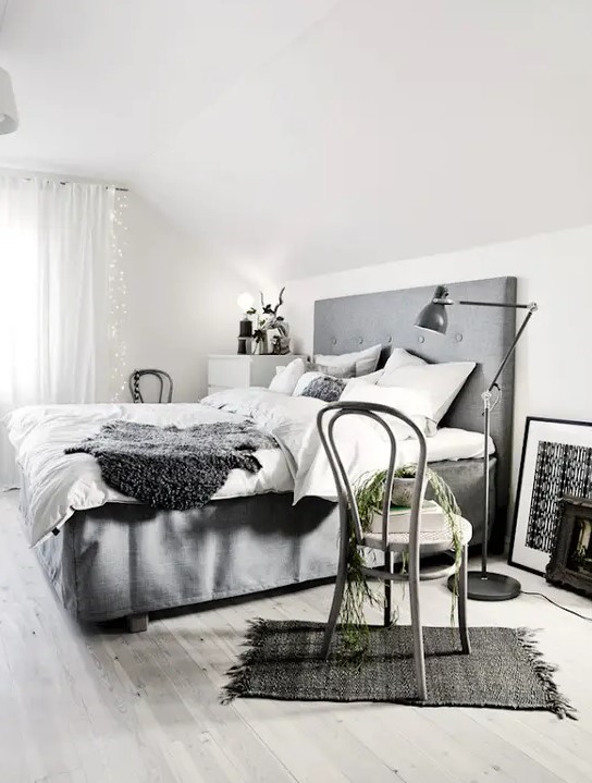 a Scandinavian bedroom with a grey bed, some retro furniture, lamps and lights hanging on the window