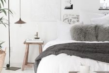 a Scandinavian bedroom with a white bed, some wooden furniture, pendant lamps, artworks and potted greenery