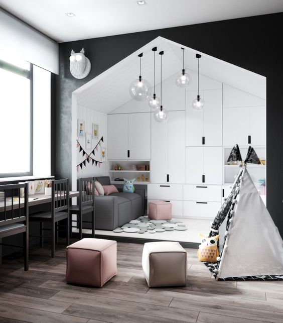 a Scandinavian kids’ room with a house-shaped niche with storage units, a grey sofa, a shared desk, a teepee and some pastel ottomans
