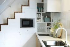 a Scandinavian kitchen with lower timber cabinets, a staircase consiting of white storage compartments, a shiny tile backsplash and spotlights