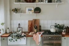 a Scandinavian kitchen with pale green shaker cabinets, butcherblock countertops, a white square tile backsplash and open shelves
