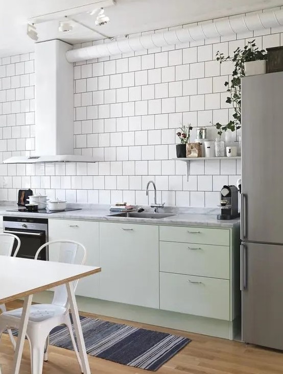 a Scandinavian kitchen with white square tiles, mint green cabinets, stainless steel appliances and white chairs and a table