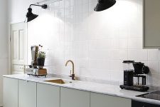 a Scandinavian kitchen with white walls and white square tiles, a row of olive green cabinets, black sconces