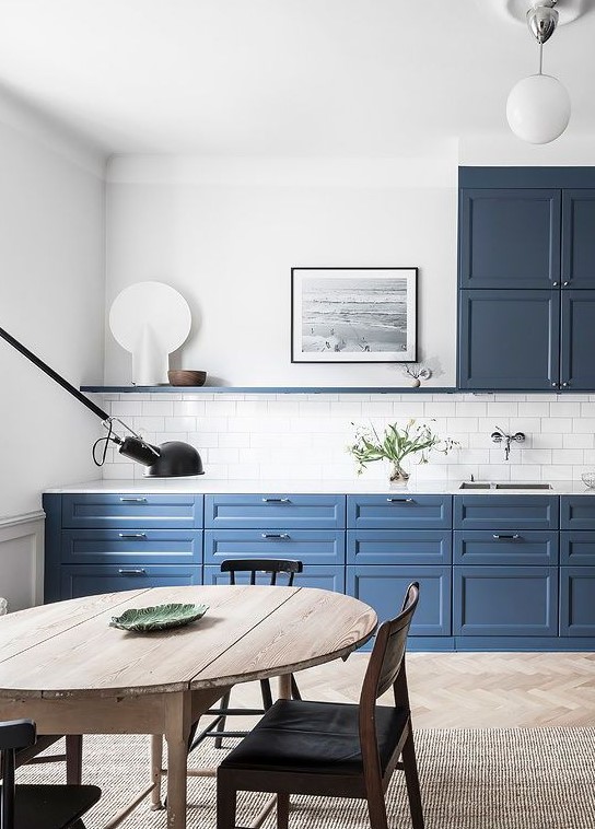 a beautiful and airy blue kitchen with a white subway tile backsplash, a stained table and black chairs