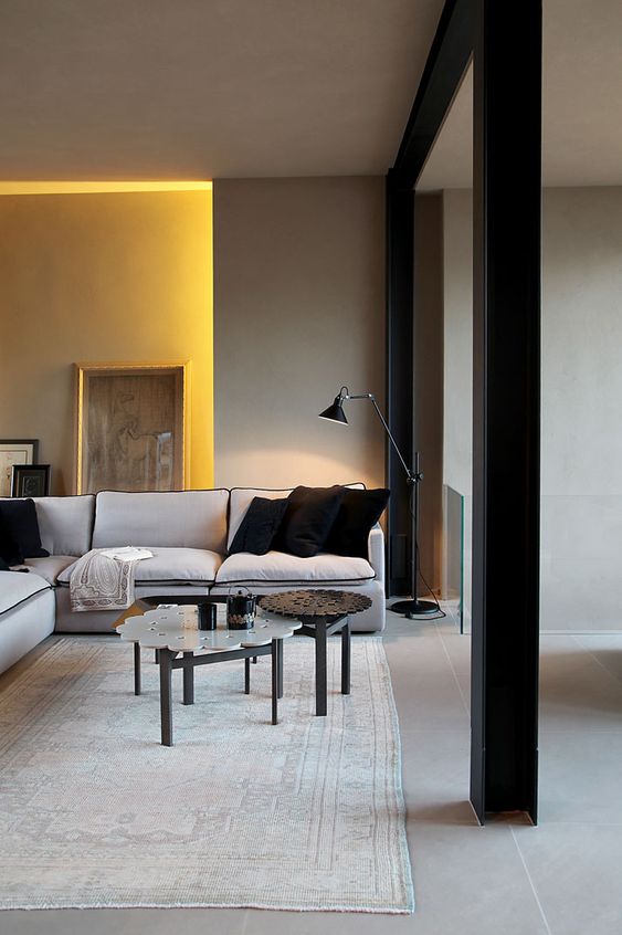 a beautiful minimalist living room with grey walls, a yellow niche, a stylish grey sectional, some pretty coffee tables and black pillows