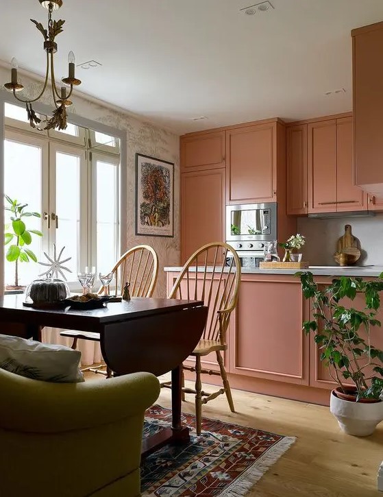 A pretty peachy pink kitchen features a handy island and built-in appliances. The dining area has a space-saving folding table. This setup is perfect for small, stylish spaces.