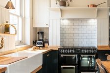 a black and white farmhouse kitchen with a white subway tile backsplash, butcherblock countertops and brass sconces