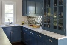a blue U-shaped kitchen with white stone countertops and a mirror tile backsplash is a very stylish space