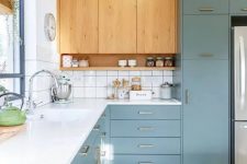 a blue and light-stained kitchen with a white countertop plus a white tile backsplash and gold and brass handles