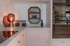 a blush L-shaped kitchen with shaker cabinets, white stone countertops, an open shelf, built-in appliances and some lovely decor