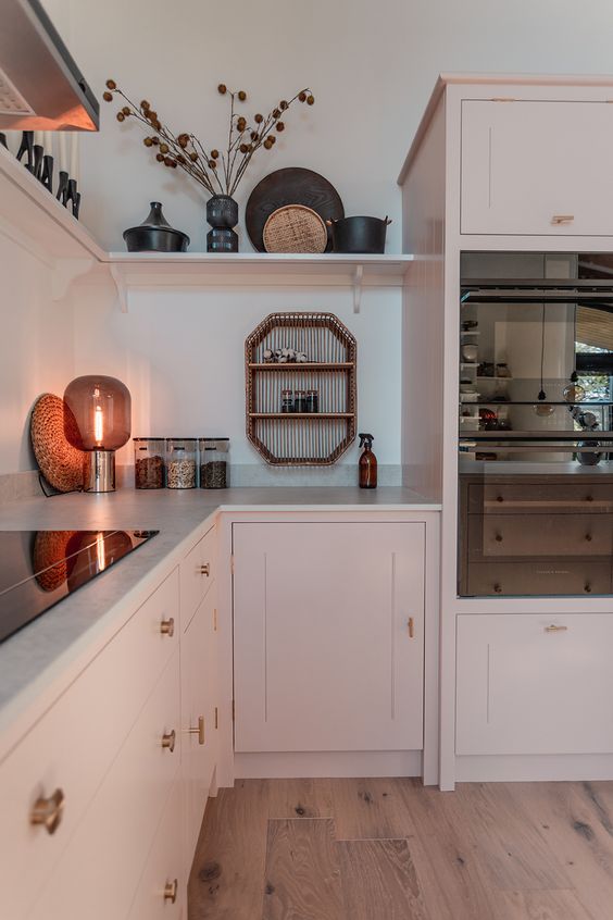 A blush L shaped kitchen with shaker cabinets, white stone countertops, an open shelf, built in appliances and some lovely decor