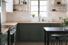 a bold green and white L-shaped kitchen with butcherblock countertops, open shelves and brass touches is very cozy
