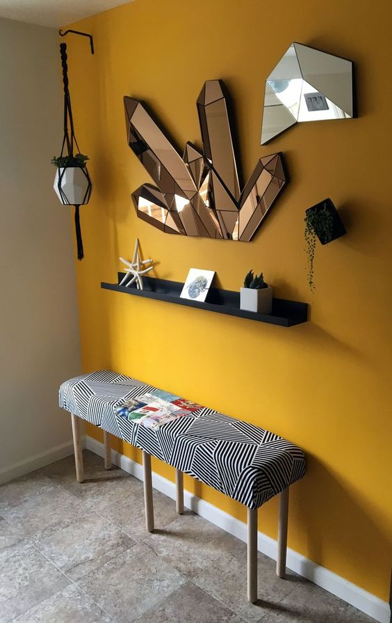 a bold modern entryway with a yellow accent wall, crystal-like mirrors, a printed bench and some potted plants