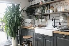 a bold modern kitchen in black, butcherblock countertops, a white subway tile backsplash and potted greenery plus open shelves