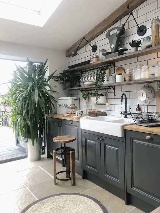 A bold modern kitchen in black, butcherblock countertops, a white subway tile backsplash and potted greenery plus open shelves.