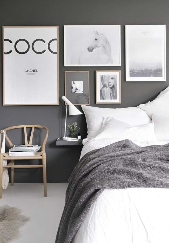 a bold monochromatic bedroom with a dark wall, lots of artworks, a comfy bed, a chair and floating nightstands
