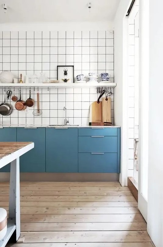A catchy blue Scandinavian kitchen with only lower cabinets, a white square tile backsplash, an open shelf and a stained kitchen island.