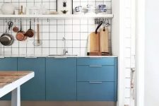 a catchy blue Scandinavian kitchen with only lower cabinets, a white square tile backsplash, an open shelf and a stained kitchen island