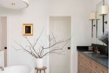 a chic Scandinavian bathroom with a stained vanity, an oval tub, a pendant lamp, a stool with branches and lamps