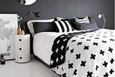 a chic Scandinavian bedroom with a black accent wall, printed bedding, a round tube nightstand and stylish lamps
