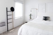 a clean Nordic bedroom with a white bed, artworks, a ladder, lamps and a stool – black for drama
