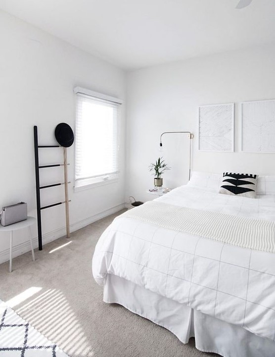 A clean Nordic bedroom with a white bed, artworks, a ladder, lamps and a stool   black for drama