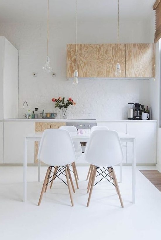 A Scandinavian kitchen features white and plywood cabinets with hanging bulbs. A sleek dining set completes the modern look. This design is perfect for a clean and simple aesthetic.