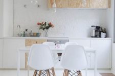 a contemporary Scandinavian kitchen with white and plywood cabinets, bulbs hanging from above and a sleek dining set