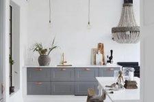 a contemporary meets vintage kitchen with grey cabinets, pendant lamps and a chandelier, a white vintage table and benches